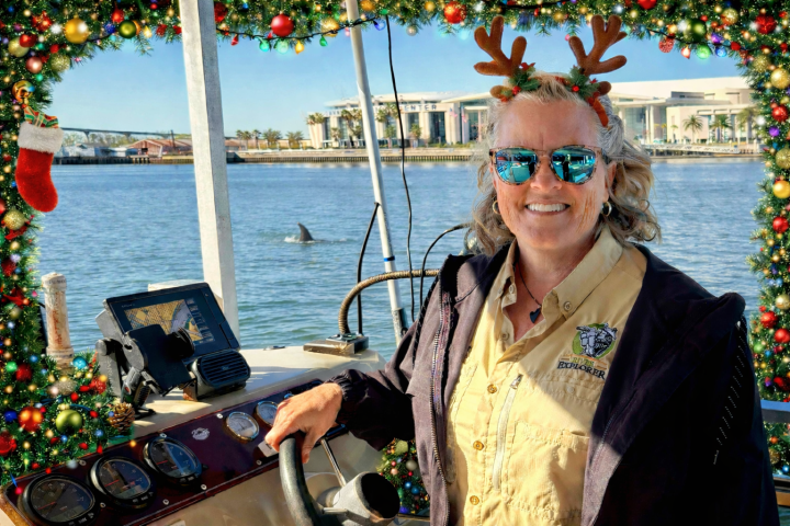 Woman wearing antler headband on a boat, with festive decor and a dolphin fin in the background.