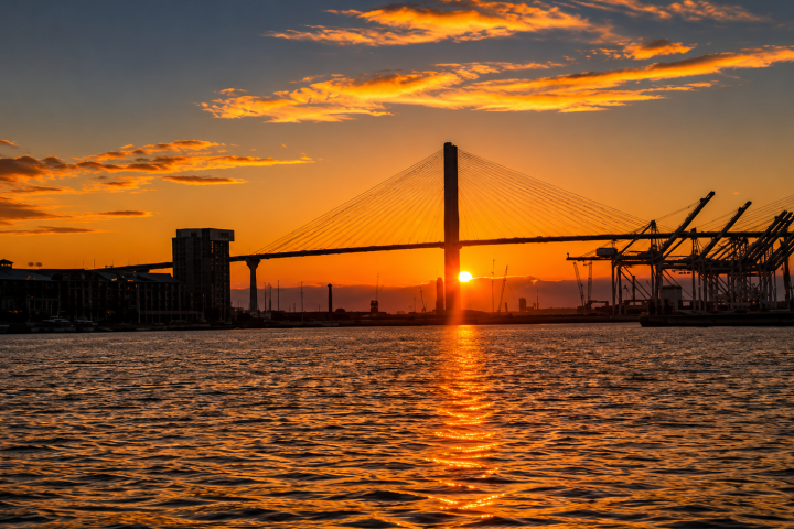 Sunset view of a bridge over water with city skyline and cranes.