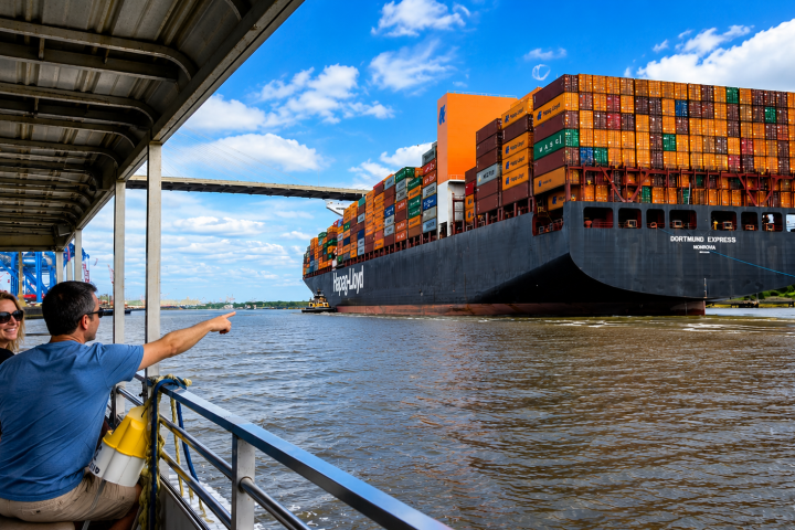 People on a boat watching a large container ship on a river.