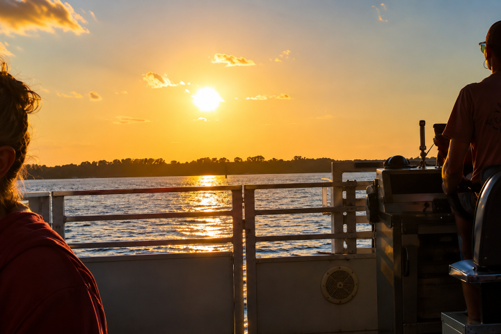 Sunset over water with people on a boat, silhouetted against the sky.