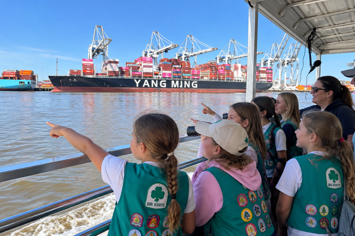 Children in green vests point at a large cargo ship named Yang Ming on the water.