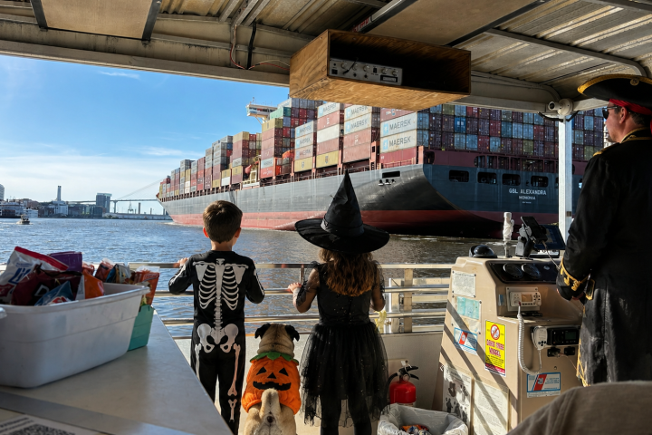 People in costumes on a boat watch large cargo ship passing by.