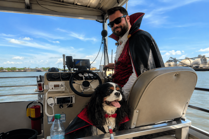 Man and dog in capes on boat, man steering.